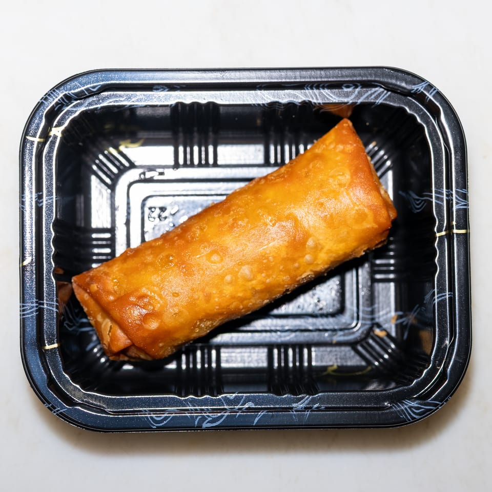 Golden fried spring roll in a black plastic takeaway container.