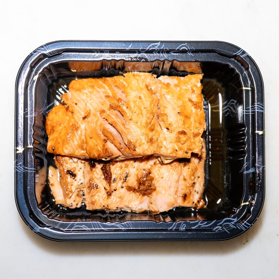 Glazed grilled salmon fillets arranged in a black takeout container.