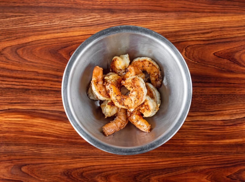 Seasoned cooked shrimp in a metal bowl on a wooden table.