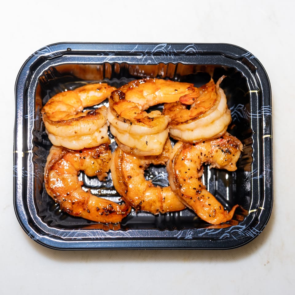 Glazed, seasoned shrimp arranged in a black takeout tray.