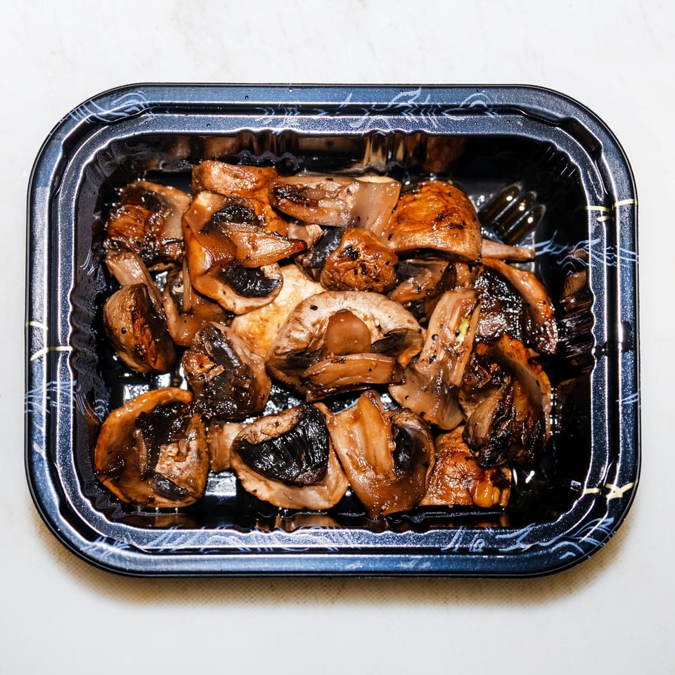Sautéed mixed mushrooms fill a black rectangular takeaway tray.