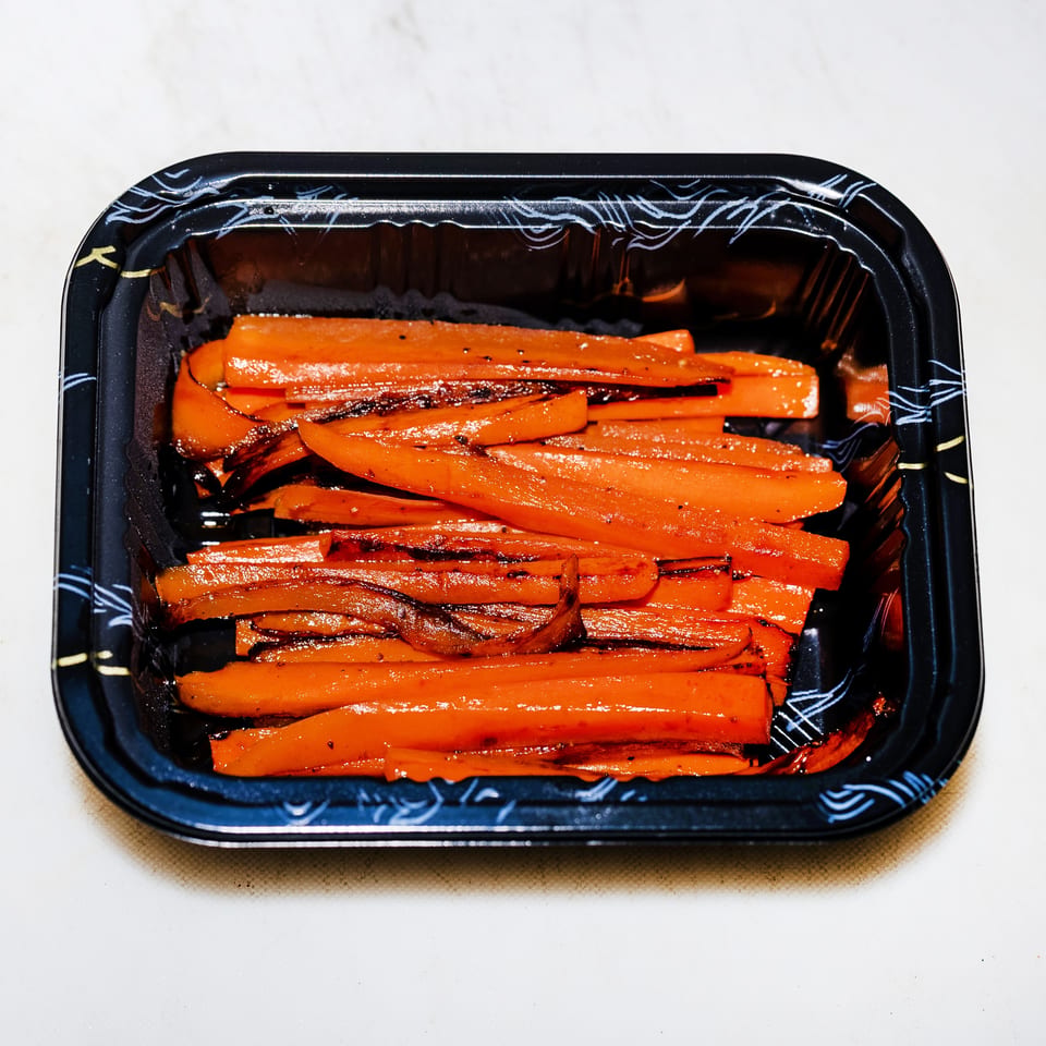 Glazed roasted carrot sticks with caramelized edges arranged in a black serving tray.
