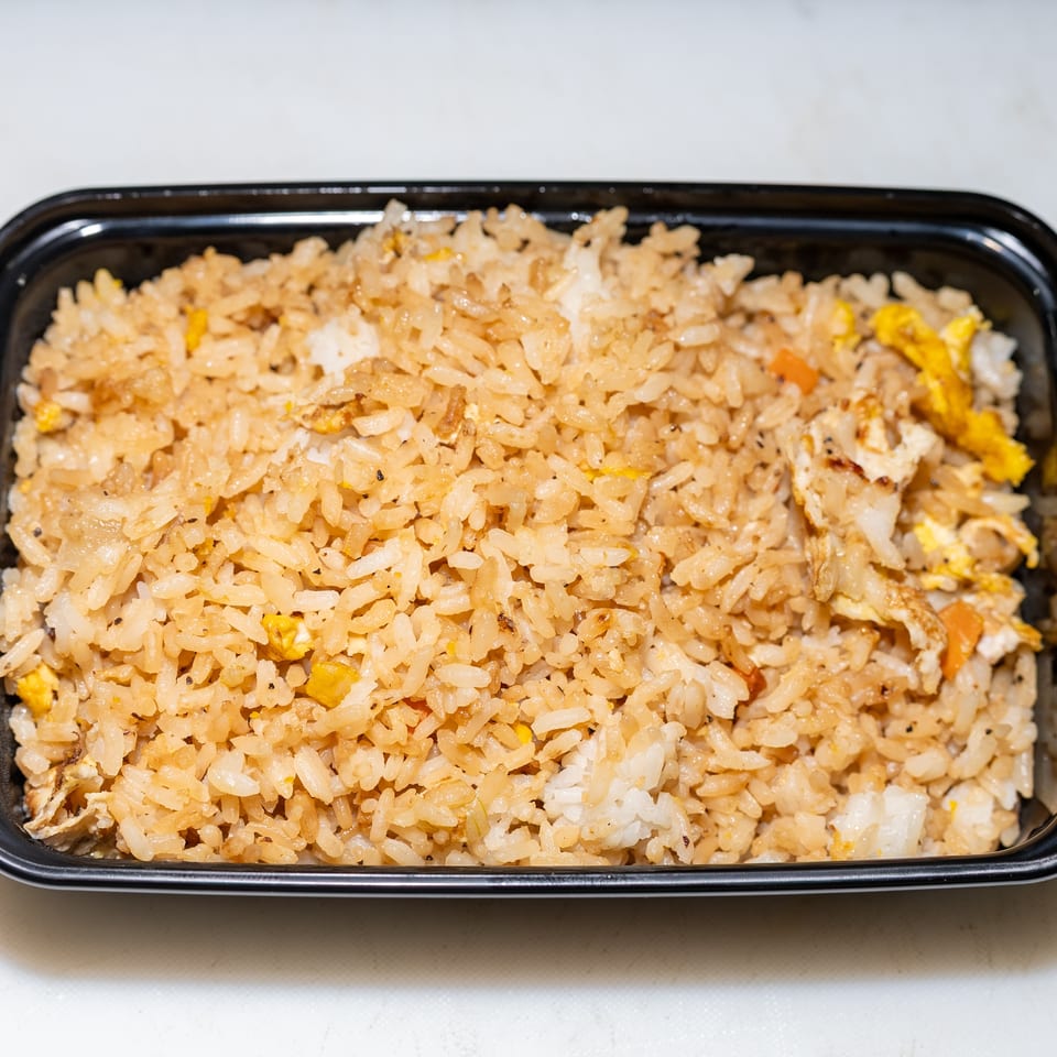 Close-up of fried rice with scrambled egg and vegetables served in a black takeout container.